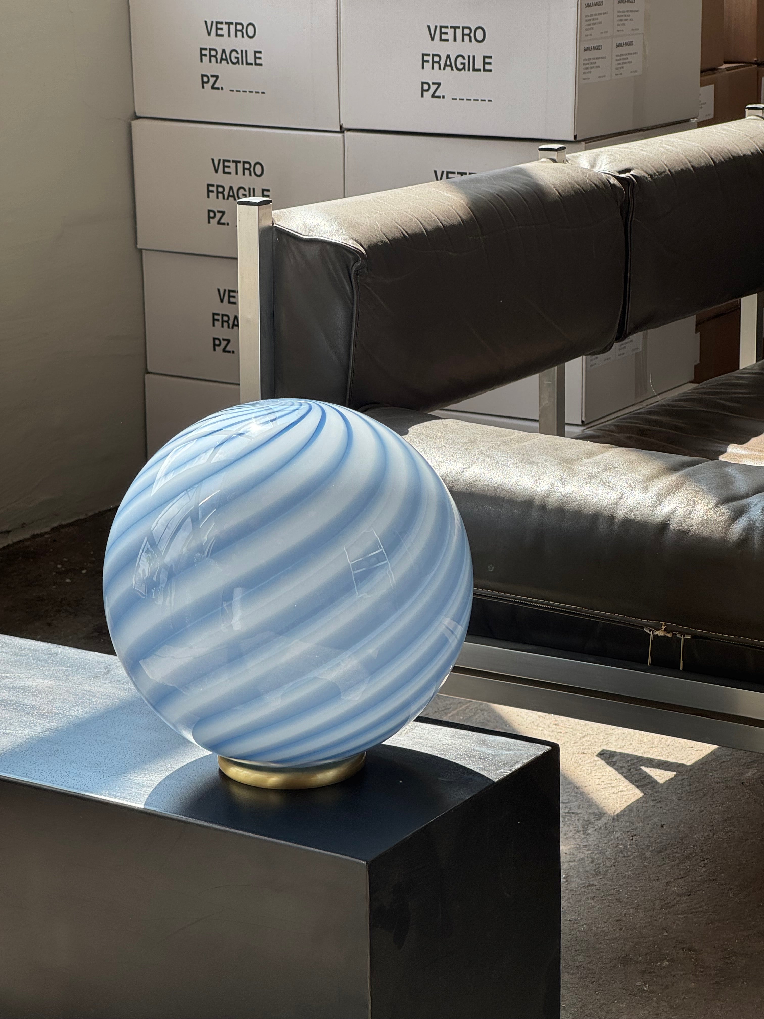 Ny Murano Candy bordlampe med blå swirl. Mundblæst glas i rund form. E27 fatning samt base med overflade i børstet messing.

Den perfekte størrelse til dit natbord, indbygget reol eller vindueskarm.