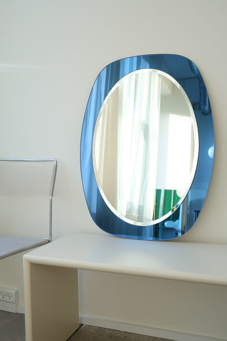 Smukt vintage italiensk vægspejl i oval glas med safir blå kant. Håndlavet i Italien, 1970erne. Glasset fremstår uden afslag/skader og er i virkelig fin stand. Kom forbi vores showroom og se det. Perfekt størrelse til badeværelse eller entré. 