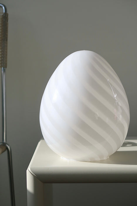 Vintage Murano egg lampe i hvid glas med swirl. Mundblæst i en smuk oval form som et æg og er derfor kendt som ''egg lamp''. Helt fantastisk, skulpturel lampe. Håndlavet i Italien, 1960/70erne, og kommer med ny hvid ledning. ⁠H: 20 cm D: 16 cm